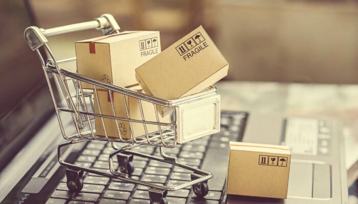 A staged photograph showing a tiny shopping cart filled with tiny boxes on top of a normal sized laptop.