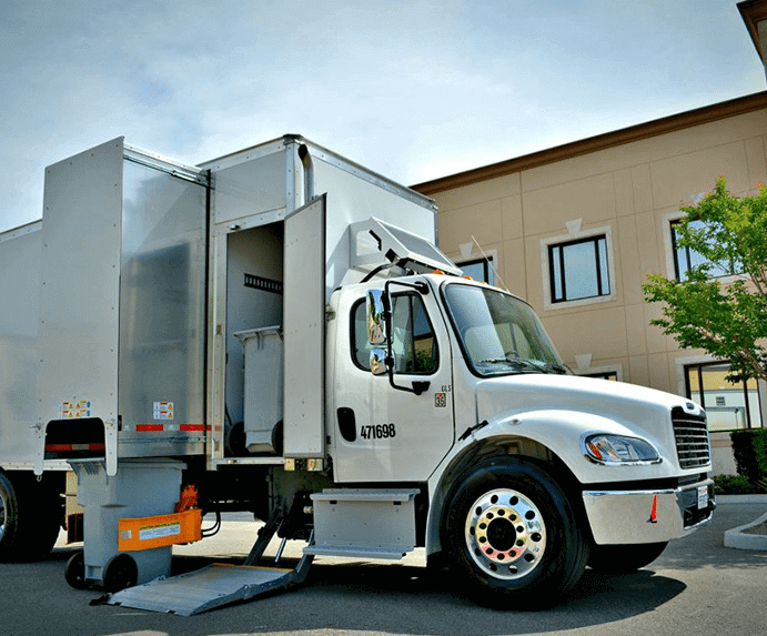 A photo of a data destruction recycling truck parked, door open and about to lift a bin into the compartment for proper disposable.
